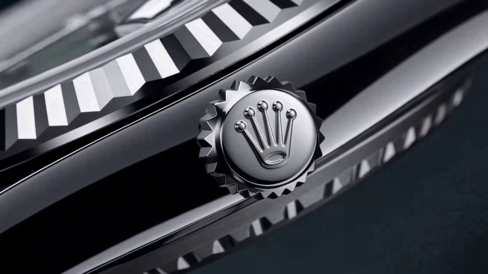 Extreme macro of a Rolex crown winder against the fluted bezel, polished steel in near-monochrome