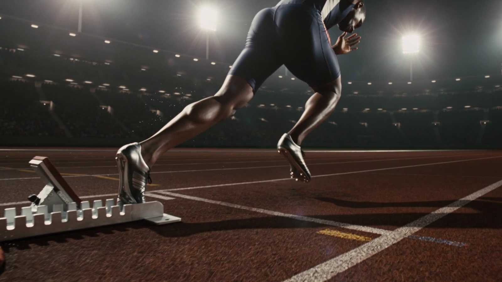 A sprinter mid-launch from the starting blocks, spikes biting the track
